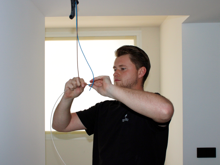 Ein Handwerker verbindet Kabel in einem Raum mit einem Fenster im Hintergrund.